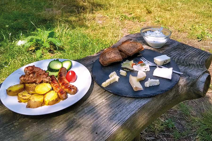 Uriger Tisch mit zwei Tellern mit Grillfleisch und Kartoffeln sowie Käse und Brot