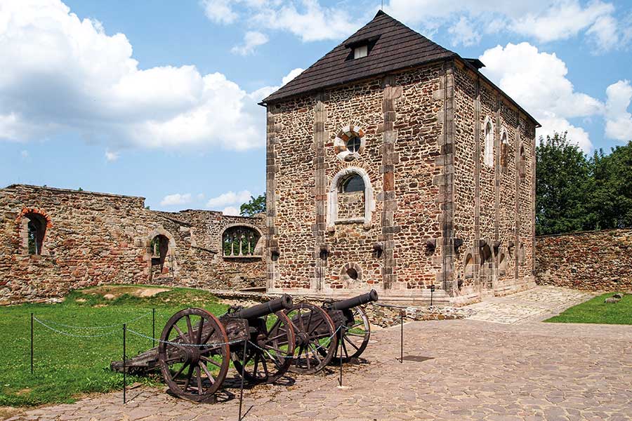 Kanonen und Burgmauer neben einem kleinen Bruchsteingebäude