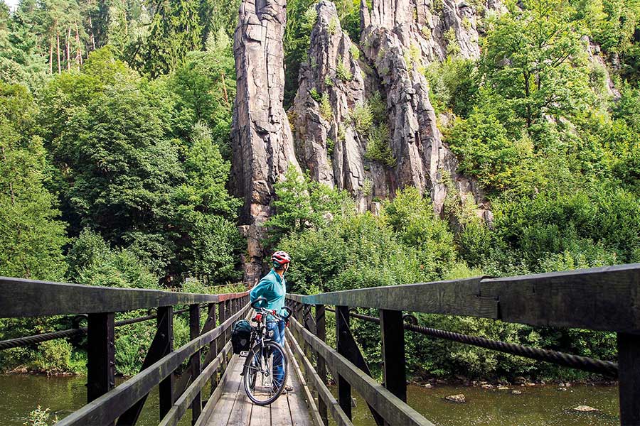 Radlerin steht auf schmaler Hängebrücke vor steilen Felsen