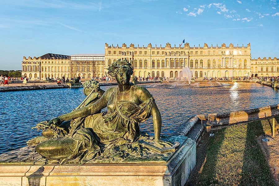 Vor der Gartenfassade von Schloss Versailles erstreckt sich ein großes Wasserbecken mit davor ein Wasserbecken mit Skulpturen