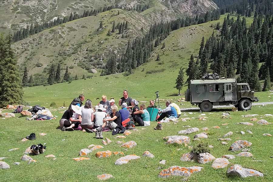 Eine Gruppe picknickt in den Bergen, daneben ein GAZ 66