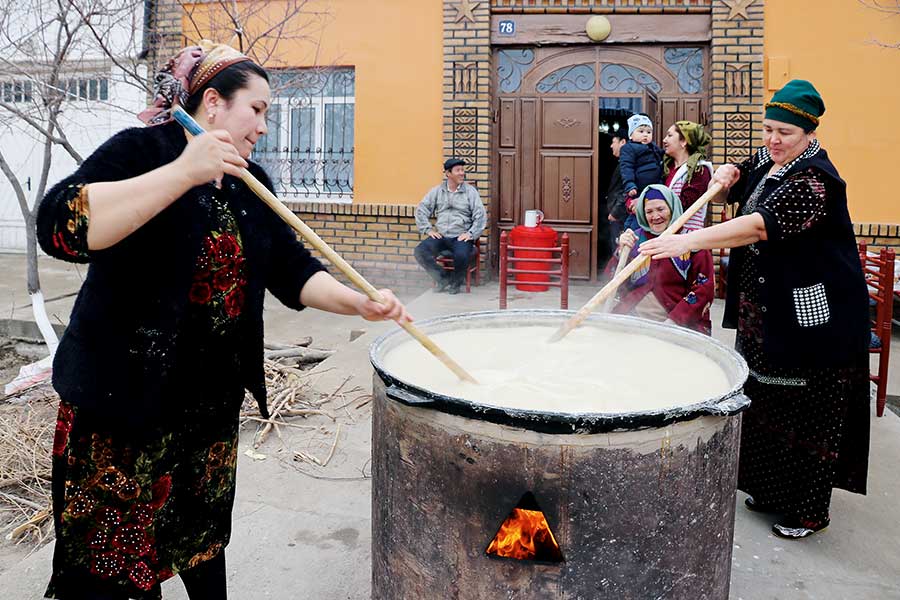 Frauen rühgren mit langen Holzlöffeln in einem riesigen Topf mit kochendem Getreidebrei