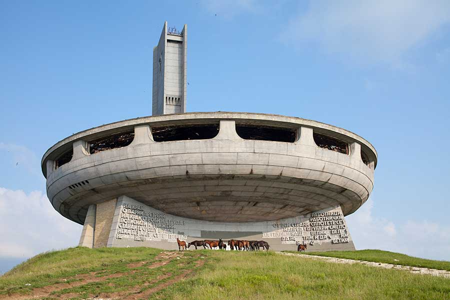 Das ufoförmige Buzludzha-Denkmal auf grünem Hügel, davor Pferde